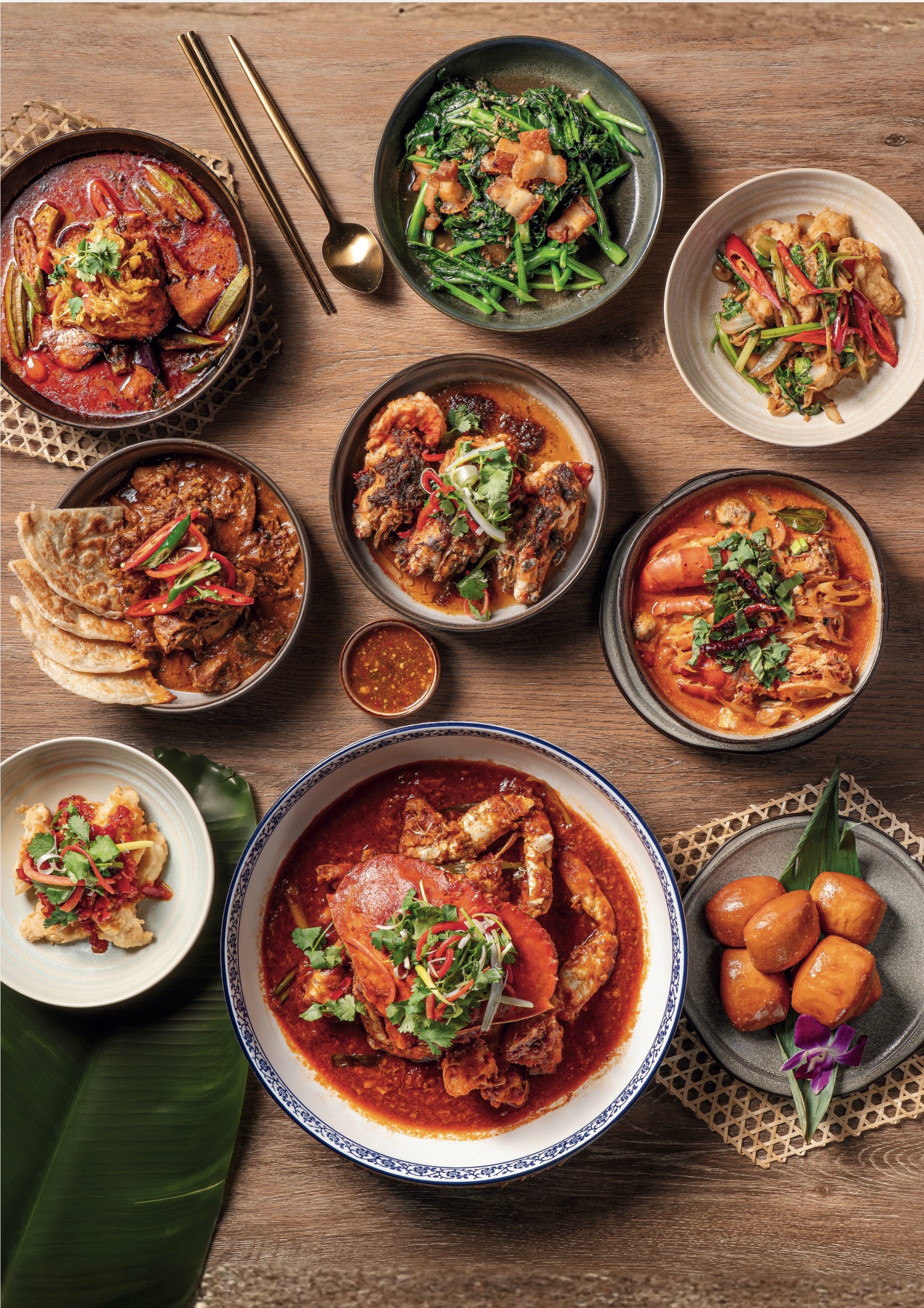 Chili crab in a blue-rimmed bowl surrounded by curries and fried buns